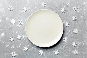 Top view of empty plate surrounded with snowflakes on cement background. New Year dinner concept photo