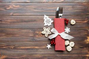 Top view of fork and knife on napkin on wooden background. Different christmas decorations and toys. New Year dinner concept with empty space for your design photo