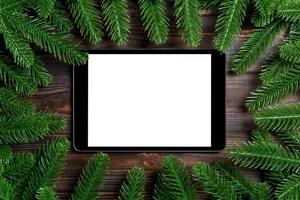 Top view of tablet decorated with a frame made of fir tree on wooden background. New Year time concept photo