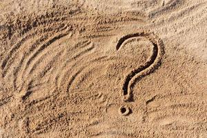 question marks written on beach sand close up, with copy space photo