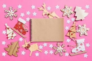 Top view of notebook, pink background decorated with festive toys and Christmas symbols reindeers and New Year trees. Holiday concept photo