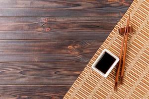 Bamboo mat and soy sauce with sushi chopsticks on wooden table. Top view with copy space background for sushi. Flat lay photo