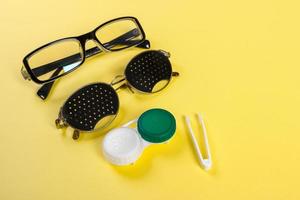 A set of accessories for sight. Pinhole glasses, lenses with container and glasses for sight. Pair of medical pinhole glasses with reflections. Medical concept. Top view photo