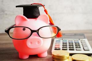 Pigging bank wearing eyeglass with coins and calculator saving bank education concept. photo