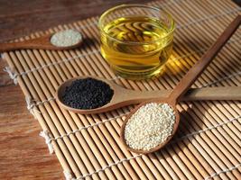 White and black sesame seeds in wooden spoon and a glass of oil. photo