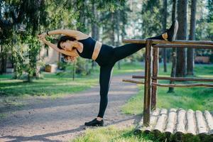 Outdoor shot of active slim young woman does stretching exercise, leans aside, keeps hands together, dressed in sportswear, breathes fresh air, leads active lifestyle. Sport and wellness concept photo