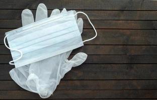 mascarilla médica blanca y guantes desechables sobre fondo de madera oscura.guantes para protección contra el coronavirus. foto