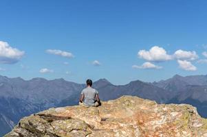 young man from the back meditating on a rock against the background of the Caucasus mountains photo