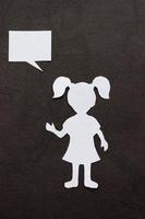 Silhouette of a girl in a dress and with ponytails made of white paper, cut by hand. On black background photo