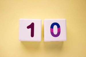 Close-up photo of a white plastic cube with a violet number 10 on a yellow background. Object in the center of the photo