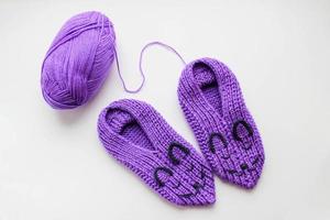 Handmade knitted pink slippers with muzzles and ball of yarn on a white background photo