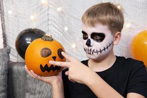 Scary child with a make-up in form of a skeleton and with a pumpkin in his hands photo