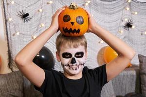 Scary child with a make-up in form of a skeleton and with a pumpkin in his hands photo