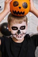 Scary child with a make-up in form of a skeleton and with a pumpkin in his hands photo