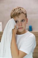 Reflection of schoolboy wiping his face with a towel after washing in bathroom. photo