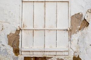 pared blanca agrietada con una ventana cerrada con persianas de madera pintadas de blanco y cerrada con dos candados foto