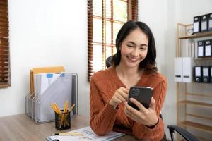 Smiling businesswoman using phone in office. Small business entrepreneur looking at her mobile phone and smiling, Young businesswoman holding a smartphone in a co-working space. photo