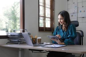 Young asian businesswoman works on tablet with laptop at the office. photo