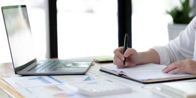 Young business woman sitting at table and taking notes in notebook.On table is laptop, smartphone photo