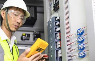 A male electrician works in a switchboard,  Electrical terminal box. Control panel with magnetic contactor and overload relay, Measuring voltage on main distribution board photo