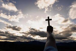 silueta de manos de mujer rezando con cruz en el fondo del amanecer de la naturaleza, crucifijo, símbolo de fe. oración de crisis de vida cristiana a dios. foto