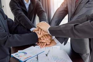 Businesspeople holding joined hands above desk with gadgets, Teamwork successful Meeting Workplace strategy with graph financial diagram top view. photo