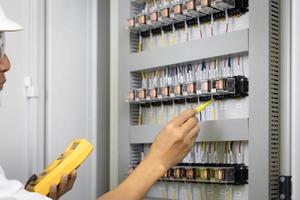 un electricista masculino trabaja en un cuadro de distribución, caja de terminales eléctrica. panel de control con contactor magnético y relé de sobrecarga, tensión de medición en el cuadro de distribución principal foto