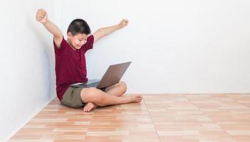 Asian boy studying online on computer laptop with smiling and happy face at home. online education and e-learning concept. photo