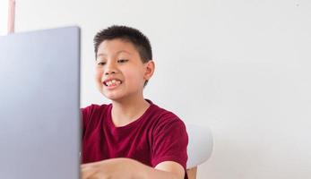 un niño lindo asiático está hablando en línea con el niño feliz de su amigo hace muecas sorprendidas y emocionadas en la computadora portátil foto