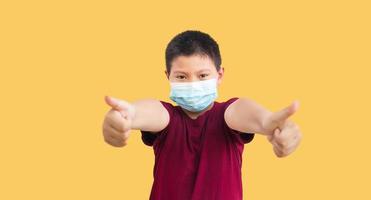 Little Asian Thai kid boy wearing face mask show thumbs up for good and happiness on white background. Covid-19 coronavirus. Stay home. Social distancing.New normal. photo