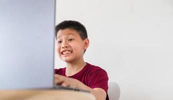 un niño lindo asiático está hablando en línea con el niño feliz de su amigo hace muecas sorprendidas y emocionadas en la computadora portátil foto