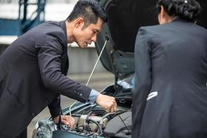 hombre de negocios ayudando a revisar y arreglar el auto de una mujer rota al costado de la carretera foto