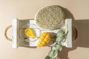 A yellow smudge of a mango body scrub, a body brush and a natural mango soap lying on a white wooden tray photo