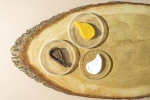 Three cosmetic smudges of body scrub and a face cream lying on a wooden plate photo