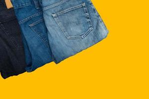 Folded denim trousers, Blue and black jeans isolated on yellow background. photo