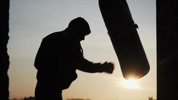 Silhouette Boxer vor dem Hintergrund eines wunderschönen Sonnenuntergangs trifft einen Boxsack schnell zum Scheitern. Müdigkeit, kann nicht mehr trainieren. Motivation. Sport und Kampfsport. video