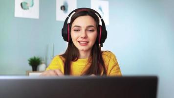 Happy woman in headphones is engaged e learning by web cam chat at home. Young female student in yellow sweater on laptop communicate online by video call. Distance education and Modern tech concept.