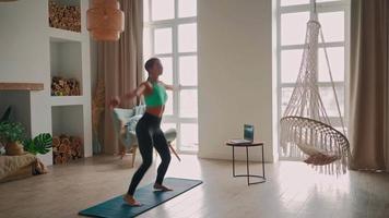 femme athlétique en vêtements de sport faisant des exercices de fitness en sautant avec l'aide de son instructeur en ligne sur un ordinateur portable sur un tapis de yoga. séance d'entraînement cardio fille déterminée. l'amélioration personnelle. formation nationale à distance video