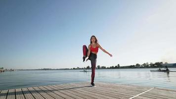 jovem garota caucasiana atlética em uma regata vermelha e legging levanta a perna na divisão. flexibilidade de alongamento. video