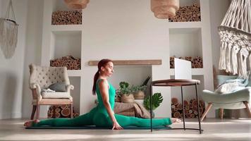 Athletic Woman in Sports Overalls doing Fitness Exercises Splits Help her Instructor Online on Laptop. Stretching Body and Yoga in Living Room. Domestic Workout Self-improvement. Training on Distance video