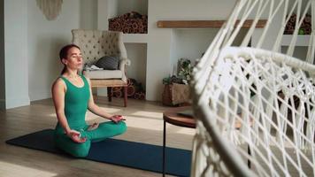hermosa mujer practica yoga y meditación en una alfombra de fitness en casa en línea a través de una computadora portátil. deportes remotos en casa. video