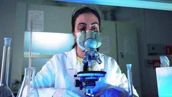 microbiólogo femenino mirando al microscopio en el laboratorio de ciencias médicas. científico, trabajando con equipos de alta tecnología. medicina farmacéutica, bioquímica, concepto científico. video