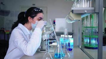 microbiólogo femenino mirando al microscopio en el laboratorio de ciencias médicas. científico, trabajando con equipos de alta tecnología. medicina farmacéutica, bioquímica, concepto científico. video