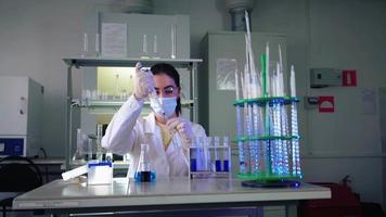 mujer científica en laboratorio haciendo experimentos químicos con líquido azul en tubos de ensayo. extracción de ADN y moléculas. desarrollo de vacunas. investigación, bioquímica, concepto de medicina farmacéutica. video