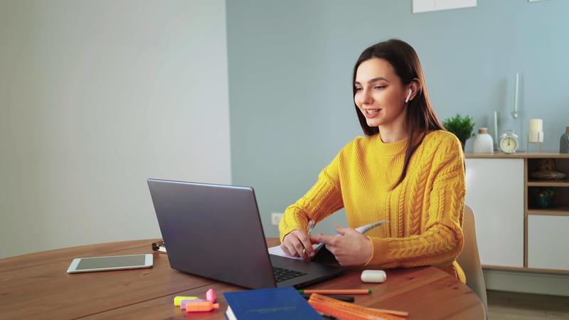 Lady student e learning using laptop webcam chat makes notes and working from home. Young pretty girl in a yellow sweater learns online with a teacher by conference call. Distance education concept. 13219560 Stock Video at Vecteezy