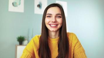 Young happy woman in yellow sweater is smiling and chatting on webcam with her followers. Female blogger makes live stream by video call with viewers. Remote communication. Social network and Internet