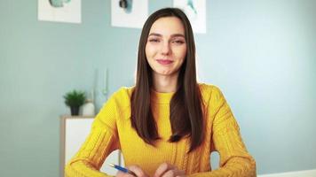 Young happy woman in yellow sweater is smiling and chatting on webcam with her followers. Female blogger makes live stream by video call with viewers. Remote communication. Social network and Internet