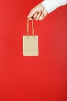 Small paper Bag at arm's length, brown craft bag for takeaway isolated on red background. Packaging template layout with space for copying, advertising. photo