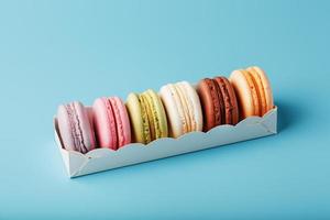 Macaroni cookies of different colors in a white box on a blue background. photo