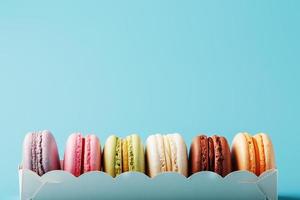 Macaroni cookies of different colors in a white box on a blue background. photo